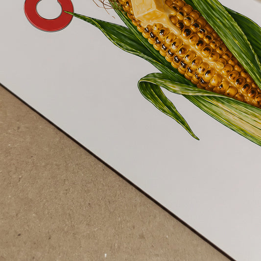 Close-up detail of the corn butter poster printed on paper, showing the edge of the artwork and the corn illustration at an angle. The image highlights the yellow kernels, green husks, red text and clean print finish. A detailed food print, corn wall art and playful kitchen poster.