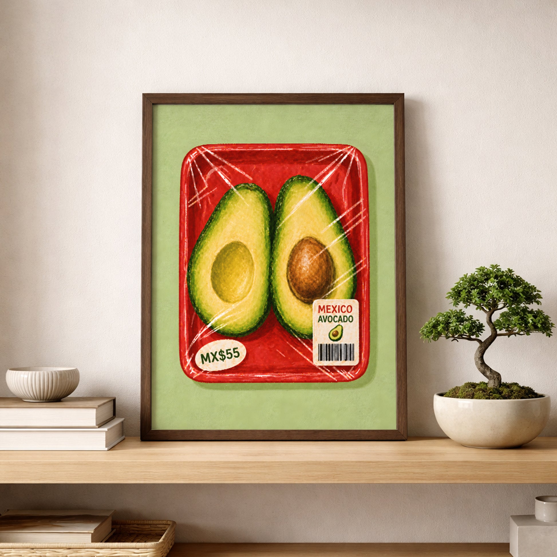 Framed Mexican avocado art print displayed on a light wooden shelf beside a small bonsai plant, stacked books and simple neutral home decor.