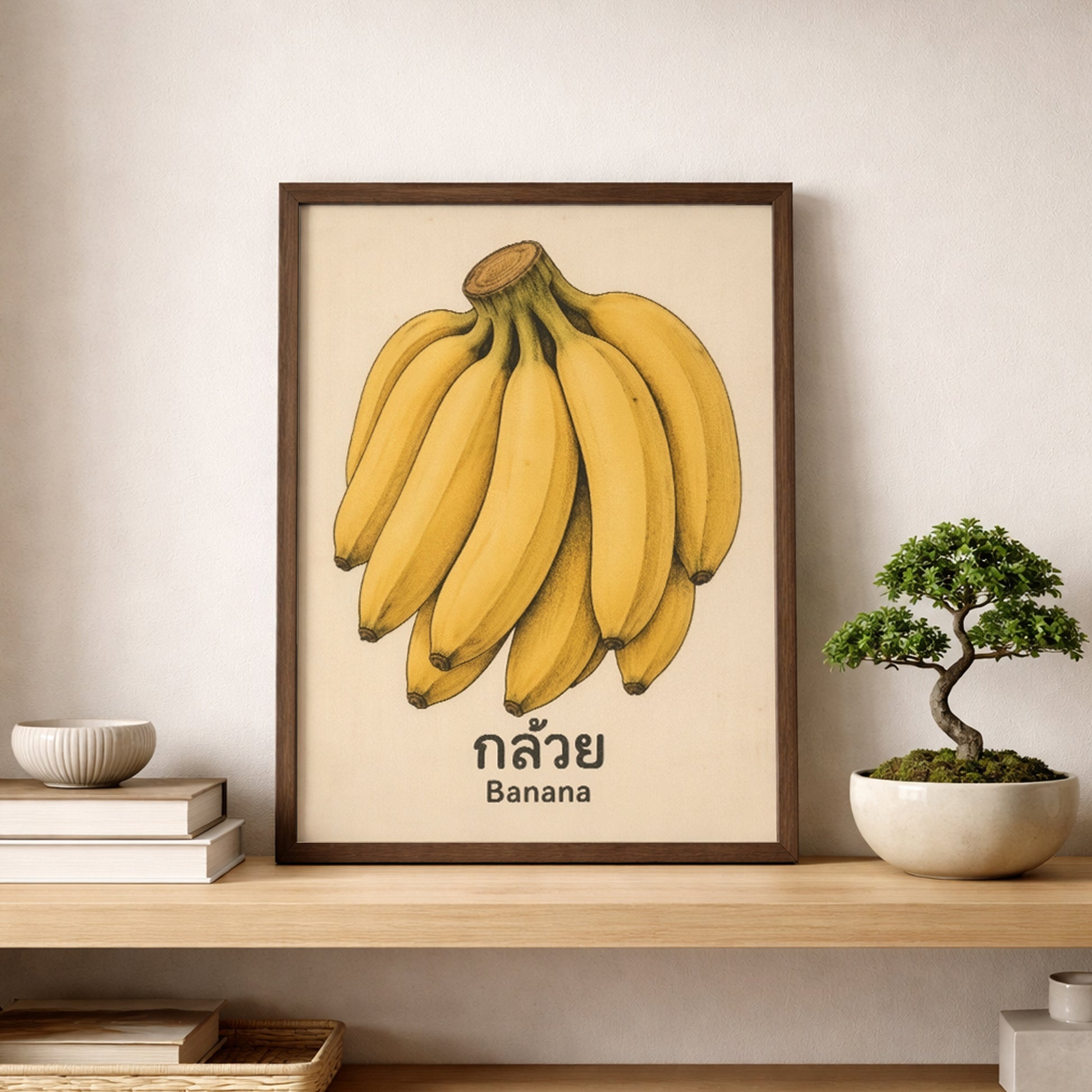 Framed banana print displayed on a shelf against a light neutral wall, styled with a small bonsai-style plant and simple home decor. The vintage Thai fruit artwork adds colour without looking too busy, with the yellow bananas and aged background keeping the look soft and easy to place. This mockup is useful for kitchen wall art, pantry decor, fruit wall print, and rustic or modern shelf styling searches.