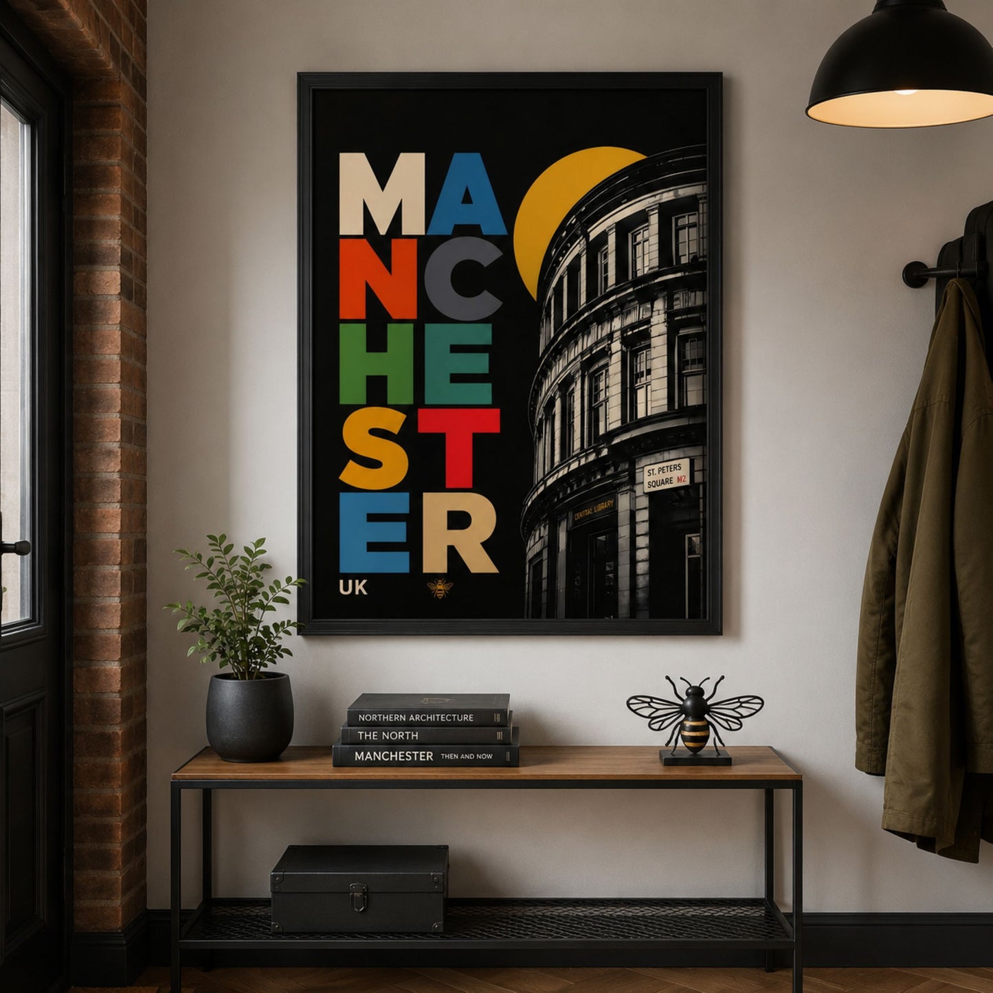 Manchester Central Library poster displayed in a black frame above a dark wood console table, with warm wall lighting, a small plant and modern living room styling.