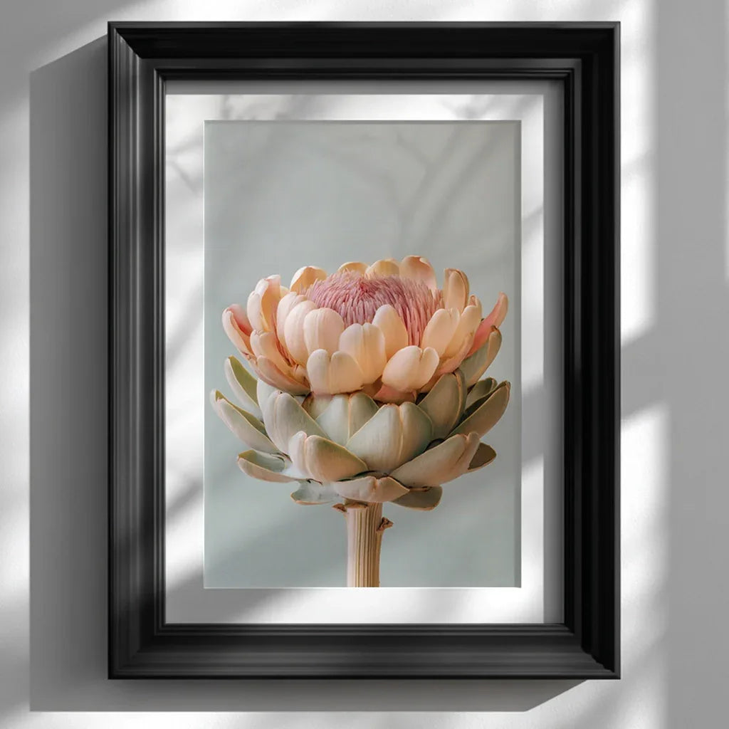 A framed pastel artichoke wall art print displayed on a clean white wall, styled in a modern black frame. Soft natural lighting and neutral décor highlight the artwork’s gentle pastel tones and botanical detail.