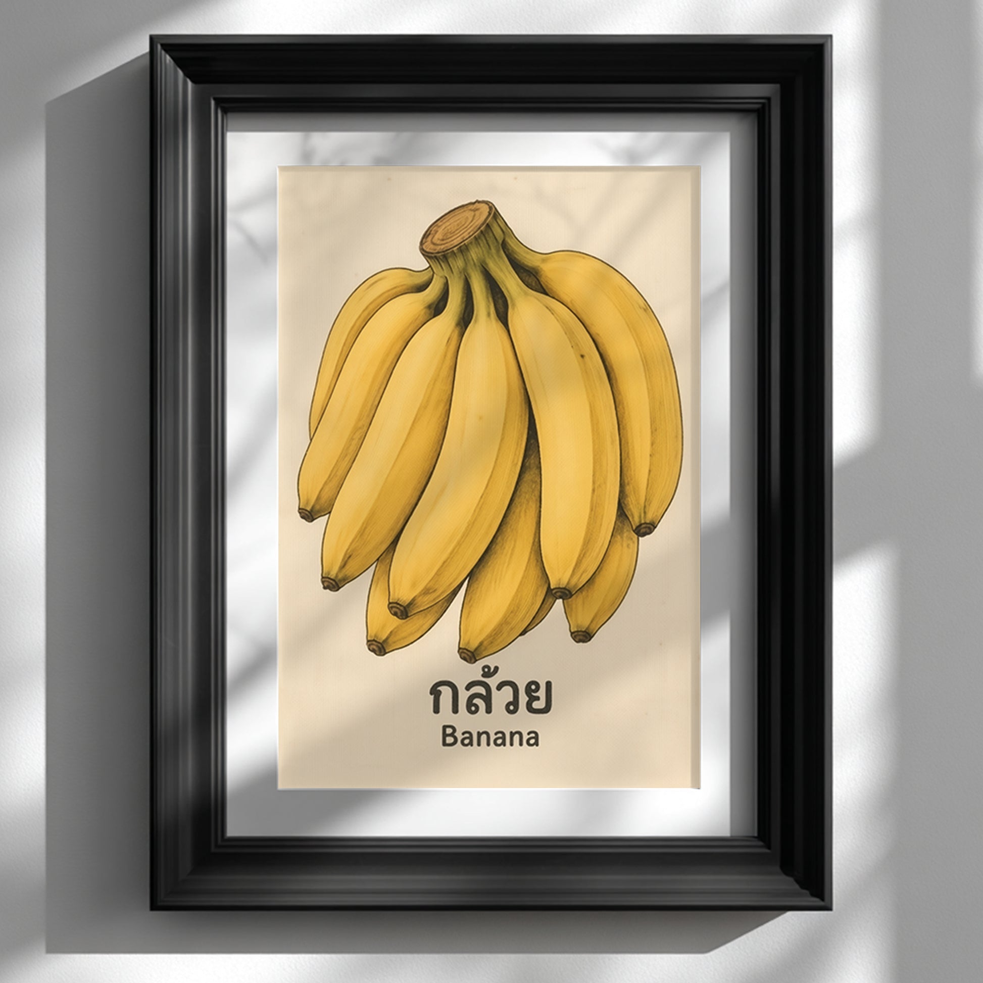 Black framed vintage Thai banana print shown hanging on a white wall. The artwork features a bunch of yellow bananas with Thai script and the English word Banana on a soft aged background. The dark frame gives the piece a sharper, more modern contrast while keeping the retro fruit poster look, making it suitable for kitchen wall art, dining room decor, or framed tropical fruit wall art.