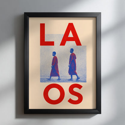 Black-framed Laos Buddhist monk poster hanging on a pale wall with soft window shadows. Oversized red LAOS lettering, blue halftone detail and two walking monks create a bold graphic focal point.