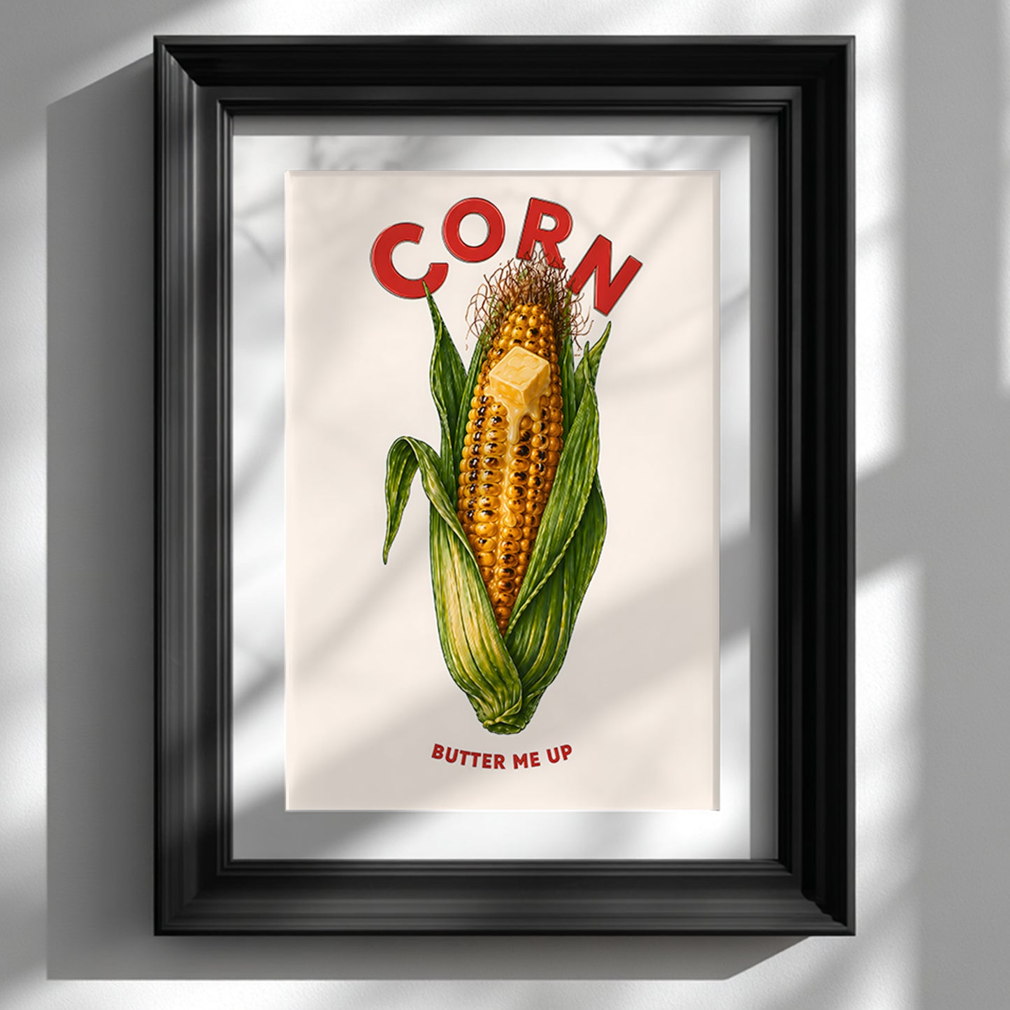 Black framed corn butter poster shown vertically on a clean white wall. The artwork features a bright corn on the cob with green husks, melting butter, red CORN lettering and BUTTER ME UP text below. A bold funny food poster for kitchens, cafés, dining rooms and playful gallery walls.