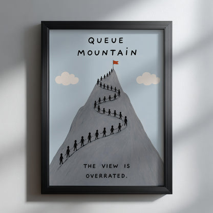 Black framed Queue Mountain poster hanging on a clean white wall, showing a grey peak with tiny hikers queuing up the mountain path, pale blue sky and cream clouds. The print reads “Queue Mountain” and “The view is overrated”, creating a funny modern hiking poster for travel-inspired decor.