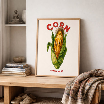 Corn butter poster styled on a shelf in a cosy room with books, soft fabric and neutral home decor. The artwork shows bright yellow corn, green husks, melting butter, red CORN text and BUTTER ME UP below. A fun food poster for kitchens, breakfast nooks, cafés and relaxed gallery walls.