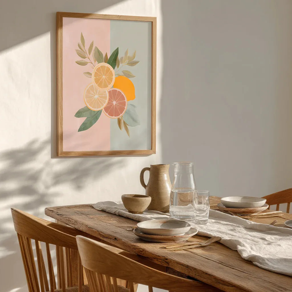 Framed pastel citrus art print with grapefruit, orange and lemon hanging above a dining table setting, styled with natural light and warm textures to show how the artwork enhances relaxed, modern home décor.