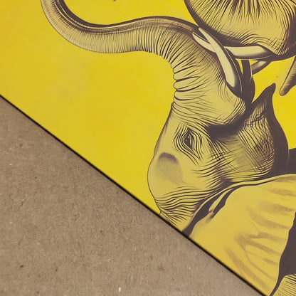 Close-up detail shot of the Elephant Heart yellow elephant print laid on a textured surface, showing the fine linework, paper edge, and part of one elephant with the curved trunk above. The bold yellow background and dark illustration give a sharp modern finish. Detail image for elephant art print, yellow elephant poster, premium paper print, and elephant wall decor listings.