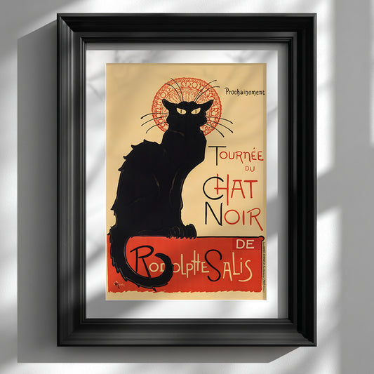 Framed Tournée du Chat Noir print by Théophile Steinlen displayed against a clean white wall in a classic black frame. The French Art Nouveau poster features the iconic black cat silhouette with yellow eyes and a red circular motif, alongside bold vintage typography. This Paris cabaret theatre poster adds striking black and red contrast to minimalist interiors and modern gallery wall decor.