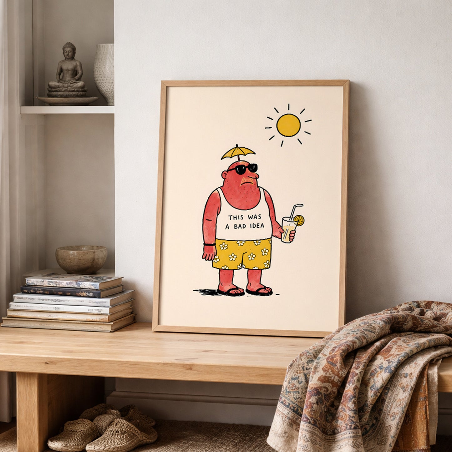 Funny travel poster in a light wooden frame on a shelf beside neutral bedding, books and simple decor. The artwork shows a sunburnt holidaymaker in sunglasses, yellow flower shorts and flip flops holding a drink under the sun, making it a dry humour travel print for bedrooms or relaxed living spaces.