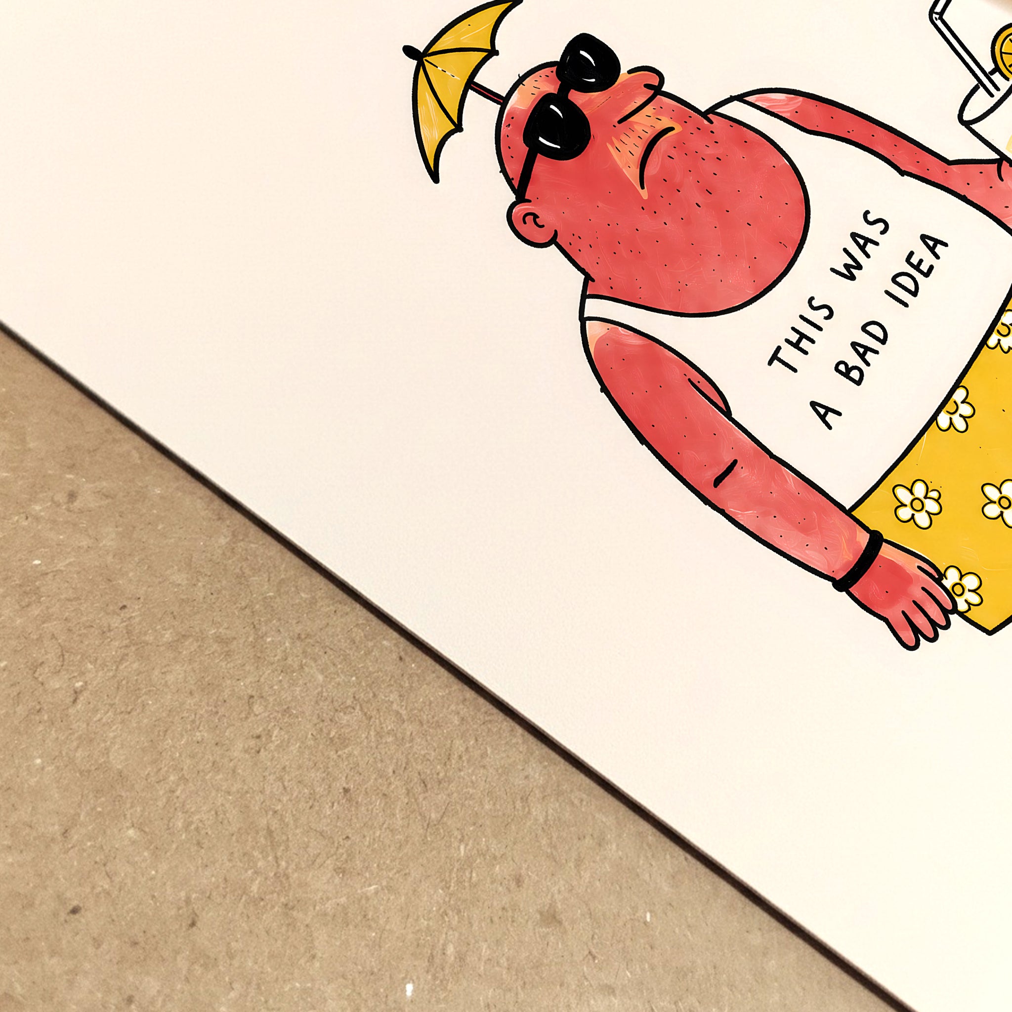 Close-up view of a funny travel poster printed on paper, showing the sunburnt cartoon character at an angle with sunglasses, a tiny umbrella hat, yellow flower shorts and a drink. The simple black linework and dry holiday joke make it a quirky summer travel print with a handmade cartoon feel.
