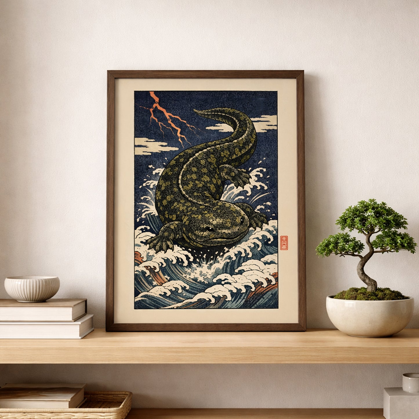 Hanzaki Japanese myth poster in a natural wood frame resting on a shelf beside a bonsai plant. The ukiyo-e inspired giant salamander rises through stylised storm waves, reflecting traditional Japanese folklore art. Cultural wall decor styled with organic elements to blend heritage printmaking with contemporary interior design.