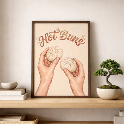Hot Buns food print displayed on a shelf in a light wood frame beside a small bonsai-style plant and neutral home decor. The artwork features steamed buns held in two hands with brown script lettering on a soft beige background. The styling gives a clean modern kitchen feel and shows how the print can work as funny kitchen wall art, foodie decor, or simple asian food wall art.
