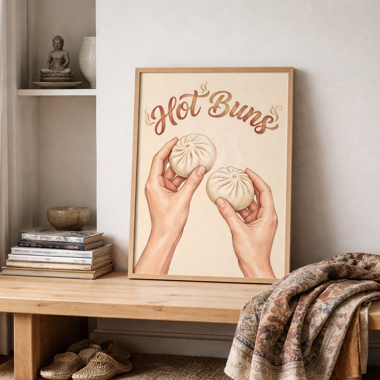 Hot Buns asian food wall art leaning on a wooden shelf in a lived-in home setting with stacked books, soft textiles, and neutral decor. The print shows two hands holding bao buns below curved brown lettering on a beige background. The overall look is calm and modern, making it easy to picture in a kitchen, dining room, breakfast corner, or restaurant style wall art setup.