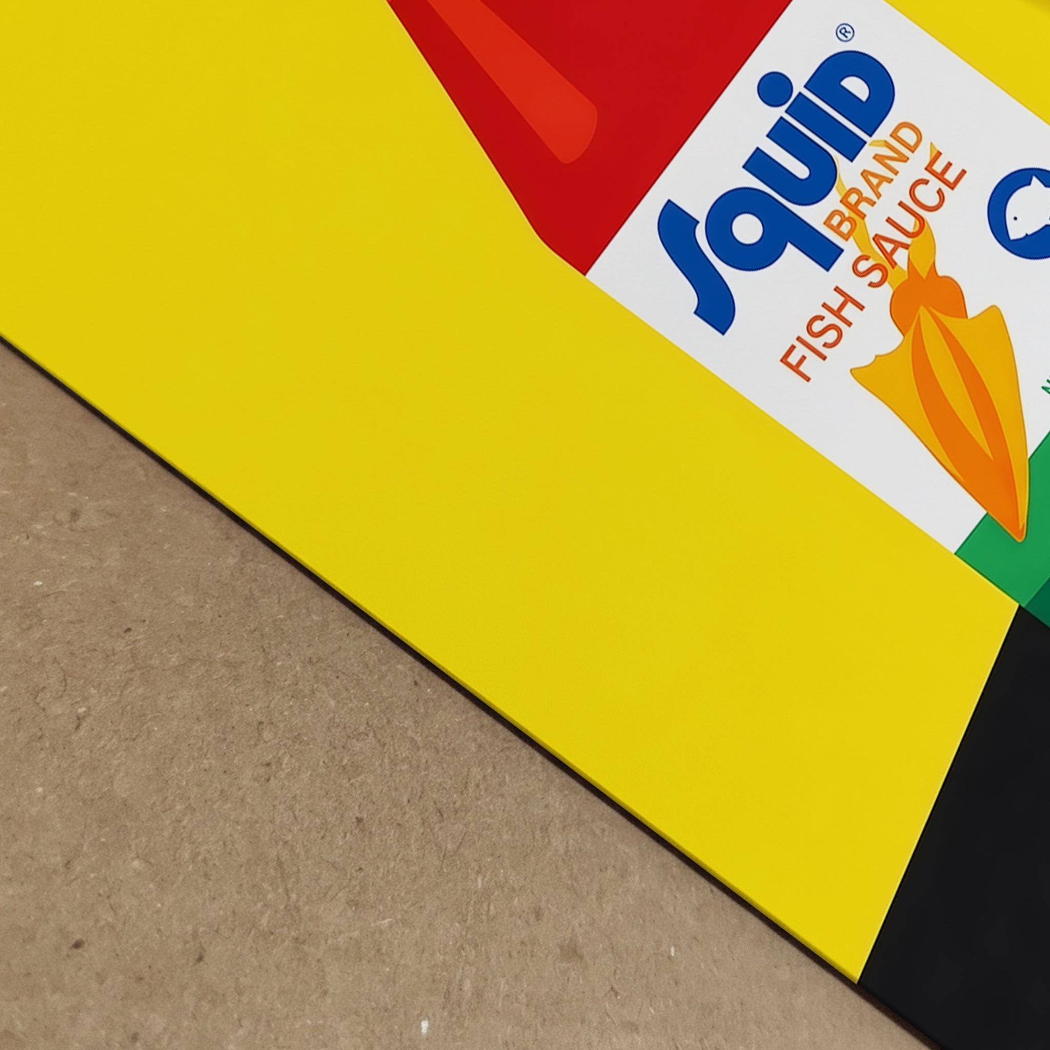 Close-up angled detail of the Squid Fish Sauce pop art poster, showing the corner of the print laid on a surface with the yellow background and partial bottle label visible. The image focuses on print texture, colour depth and the sharp graphic design elements. This detail shot is useful for showcasing the quality of the food poster, modern pop art finish and the bold Thai kitchen art styling of the print.