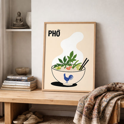 Vietnamese pho poster leaning on a shelf in a warm neutral interior beside stacked books, ceramics and a patterned textile. The food illustration features a steaming noodle bowl with herbs, lime, chilli and chopsticks.