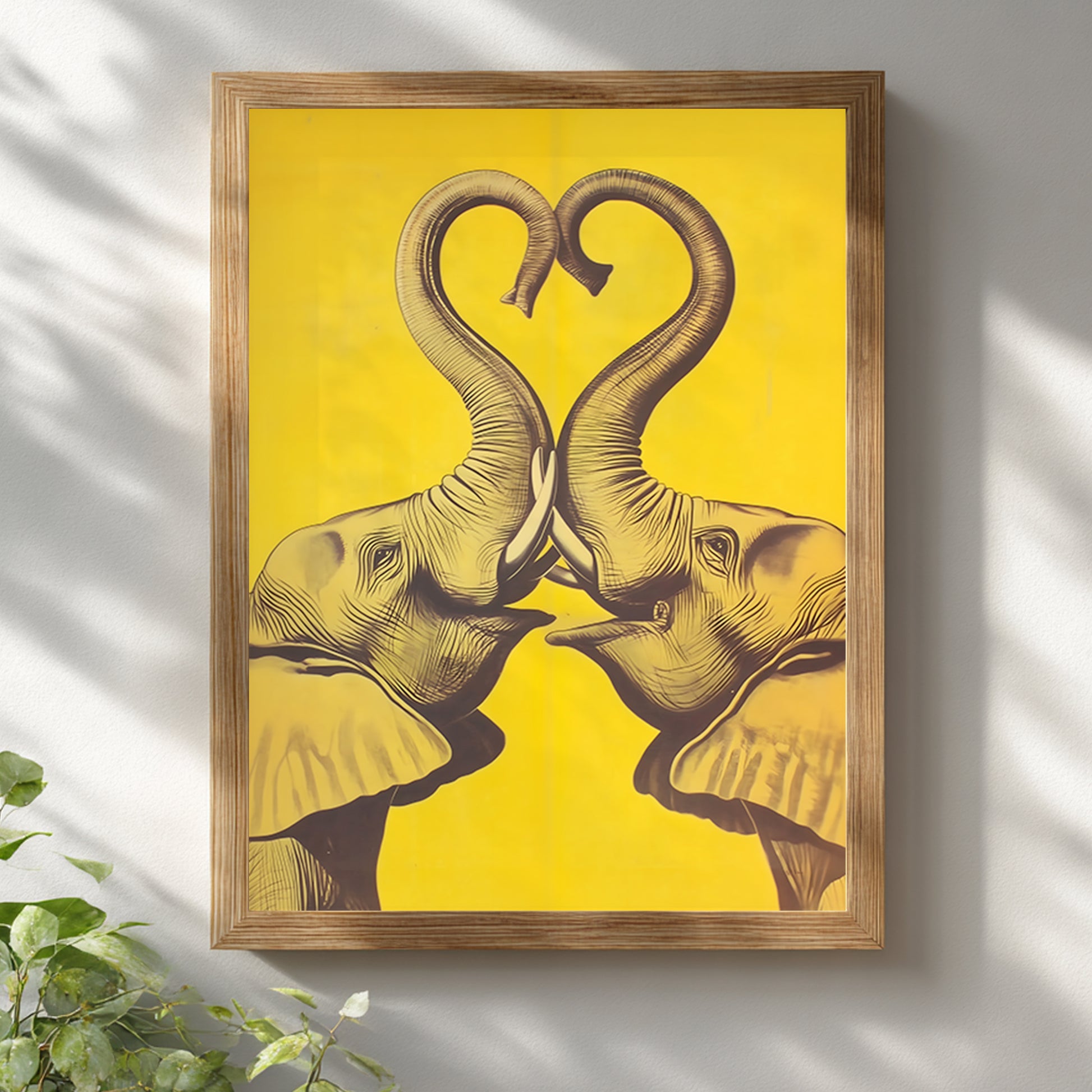 Wooden framed Elephant Heart elephant poster hung on a white wall with soft natural light and plant styling. The design shows two mirrored elephants facing inward, their trunks lifted into a heart shape in dark linework on a bold yellow background. Bright mockup for elephant wall art, elephant print, yellow elephant wall decor, framed elephant art, and modern cultural interiors.