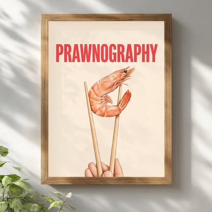 Framed Prawnography shrimp food poster displayed on a white wall in a light wooden frame with a white mount. The artwork shows a prawn held in chopsticks beneath bold red PRAWNOGRAPHY text on a soft cream background. Bright natural light and simple styling make it fit modern kitchen wall art, seafood themed decor, funny dining room prints and clean contemporary interiors with neutral tones.