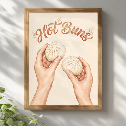 Framed Hot Buns wall art displayed in a light wood frame against a white wall with soft natural shadow. The design shows two hands holding steamed bao buns under curved brown text on a beige background, giving it a clean and playful look. Styled as modern kitchen wall art, food print decor, and a simple asian-inspired piece for dining rooms, breakfast corners, or neutral interiors.