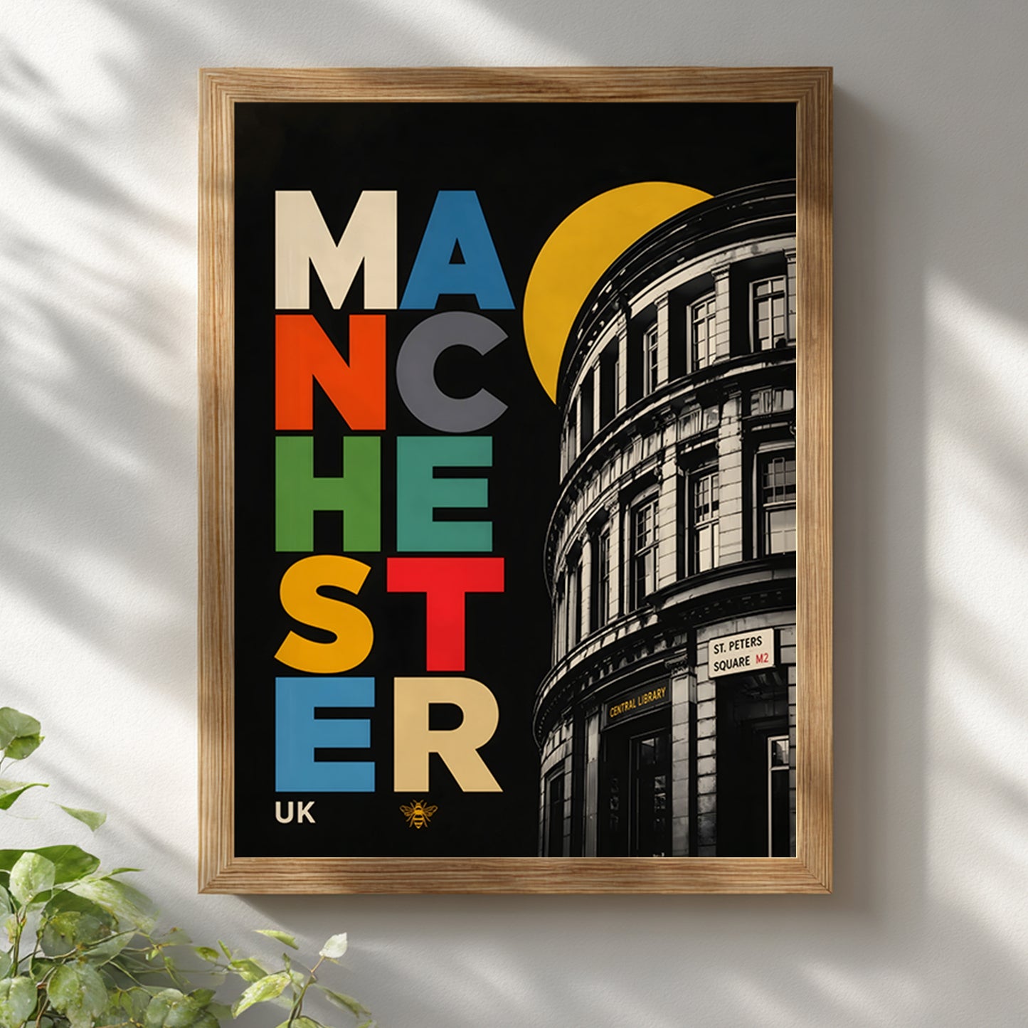 Colourful Manchester Central Library poster in a natural wooden frame on a white wall, styled with soft daylight and greenery in a bright modern home interior.