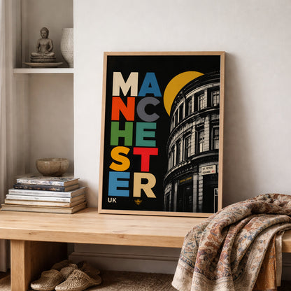 Manchester Central Library print in a wooden frame on a shelf beside neutral books and folded textiles, styled in a warm, lived-in interior with soft natural tones.