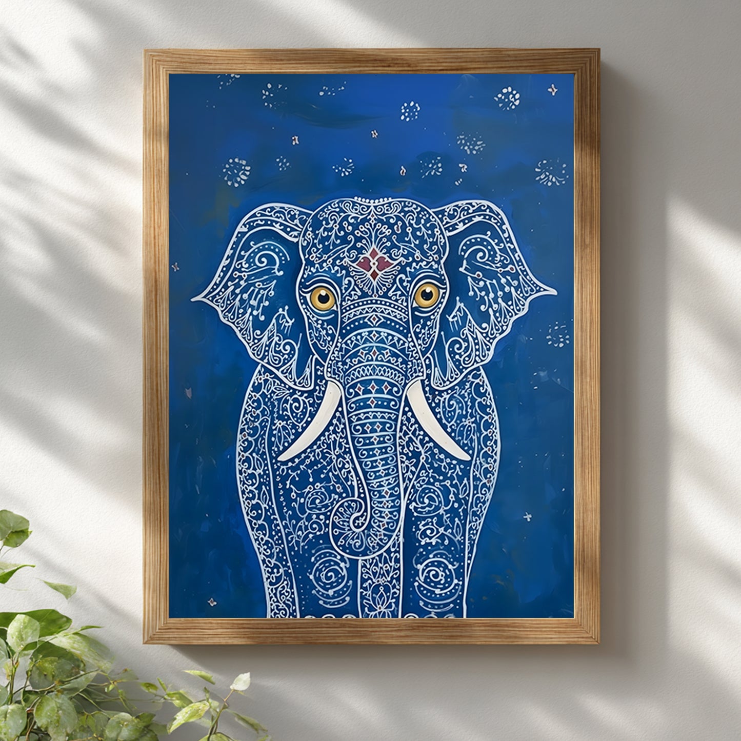 Blue Elegant Elephant Print shown in a natural wooden frame against a white wall with soft daylight shadows. The artwork features a front-facing elephant with detailed white pattern lines, gold eyes, white tusks and a small red forehead detail on a deep blue background. A clean styled mockup for blue elephant wall art, Indian elephant print and decorative animal wall decor.