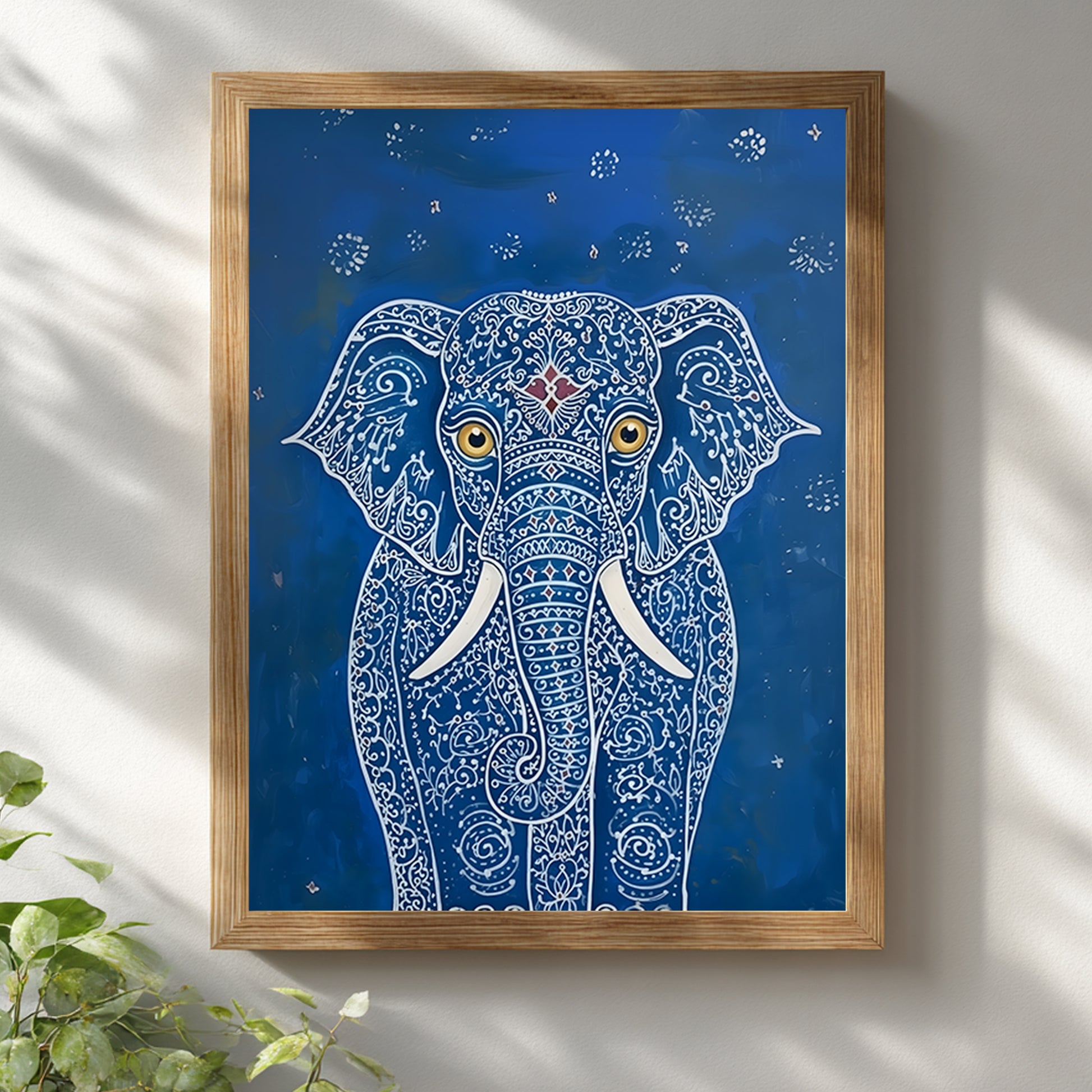 Blue Elegant Elephant Print shown in a natural wooden frame against a white wall with soft daylight shadows. The artwork features a front-facing elephant with detailed white pattern lines, gold eyes, white tusks and a small red forehead detail on a deep blue background. A clean styled mockup for blue elephant wall art, Indian elephant print and decorative animal wall decor.