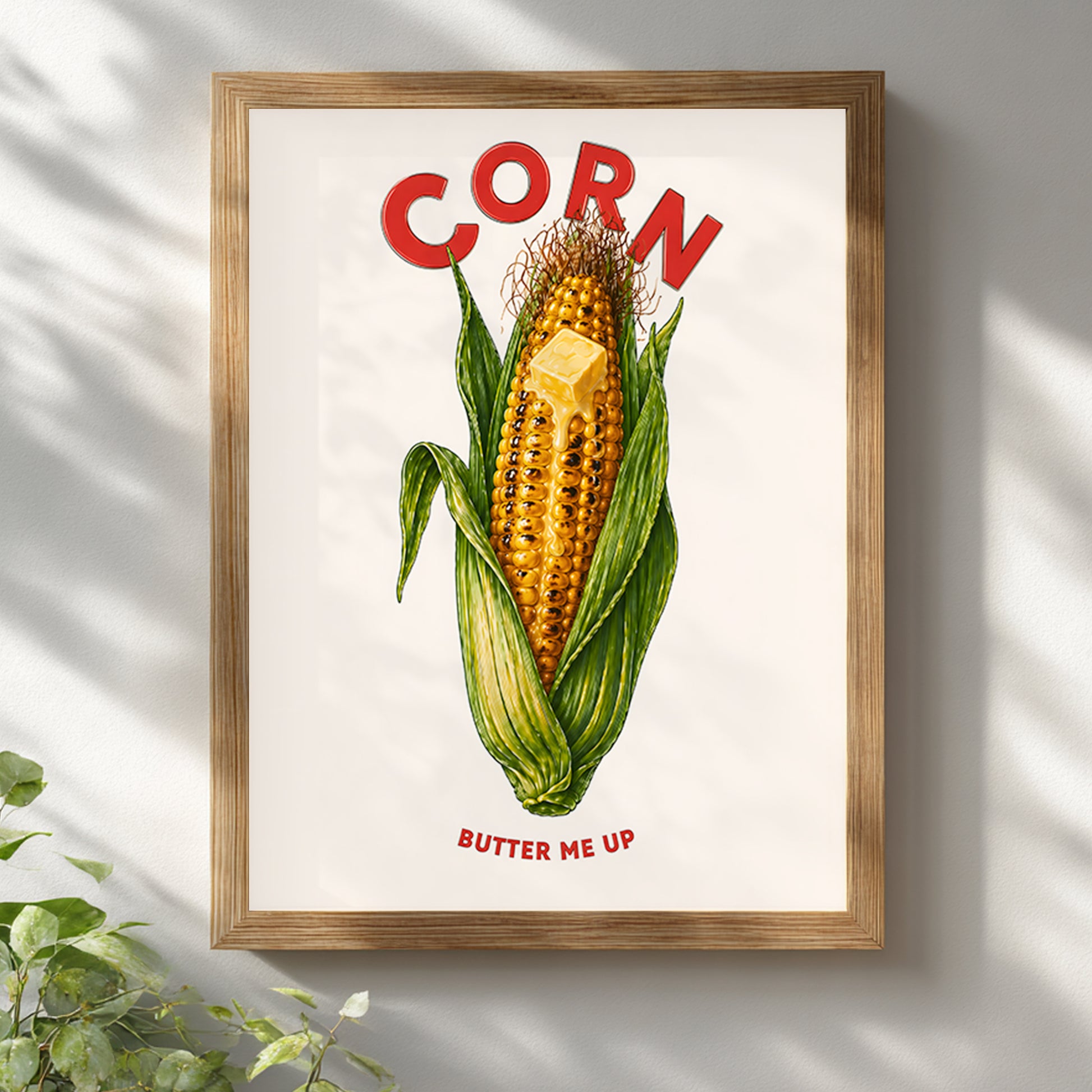 Wooden framed corn butter poster hanging on a bright white wall with soft natural light and shadow. The artwork features yellow corn on the cob, green husks, melting butter, red CORN lettering and BUTTER ME UP text. A retro food print for kitchens, cafés, dining rooms and farmhouse wall decor.