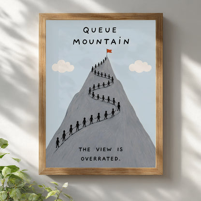 Wooden framed Queue Mountain poster hanging on a bright white wall with soft natural shadows. The artwork shows a grey mountain filled with tiny hikers queuing along a winding route, pale blue sky, cream clouds and the words “Queue Mountain” and “The view is overrated”, ideal for funny hiking wall art.